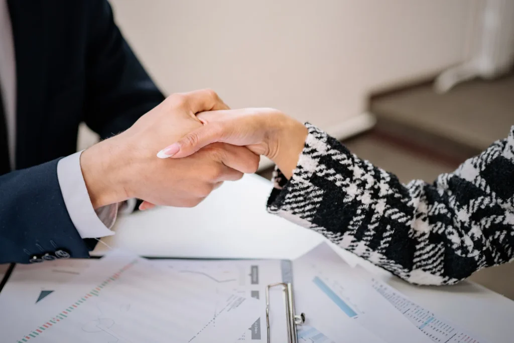 Close-up of two people shaking hands over documents during a business agreement