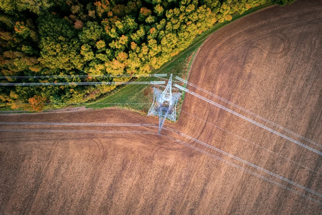 Overhead power lines crossing agricultural land and woodland from above