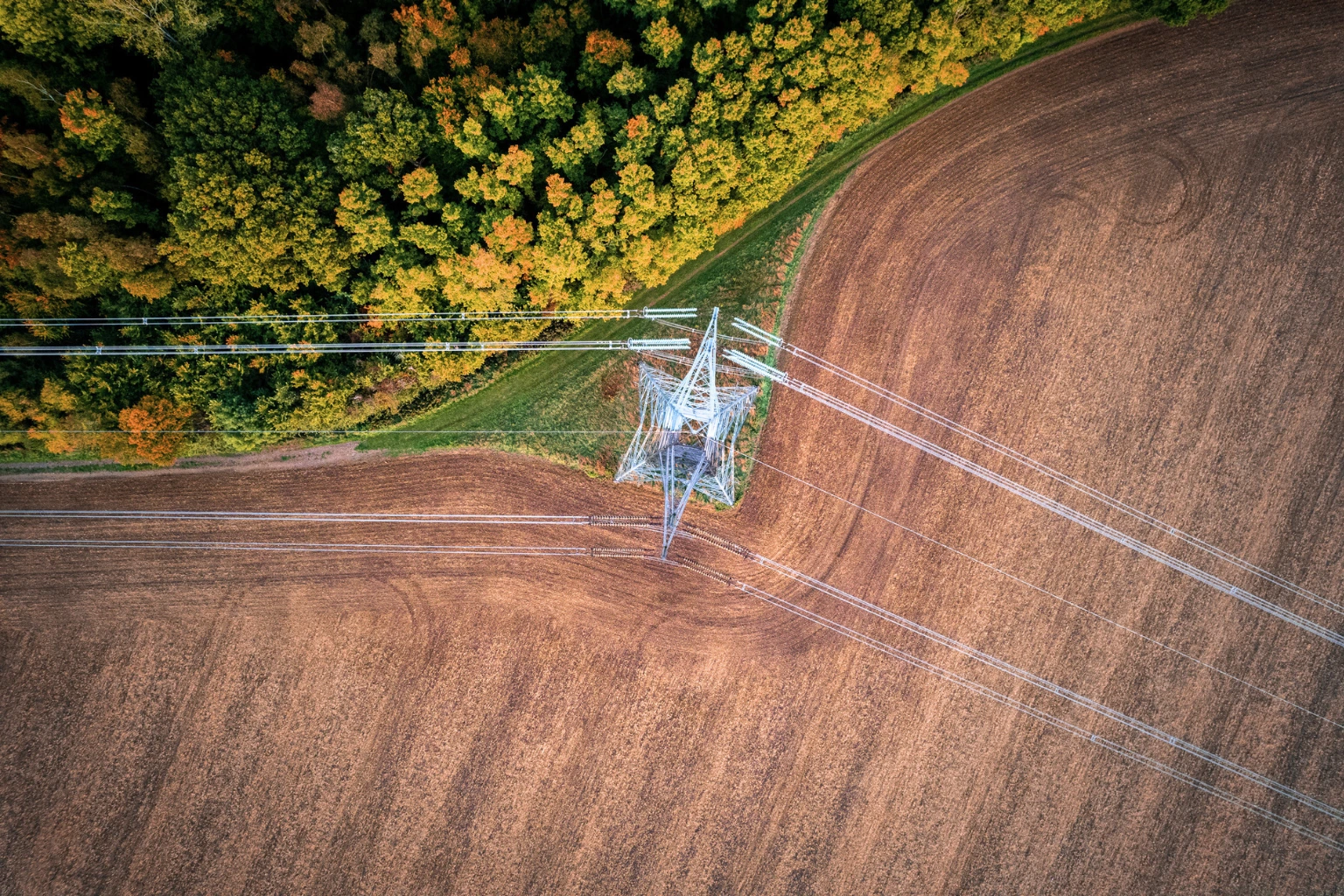 Overhead power lines crossing agricultural land and woodland from above