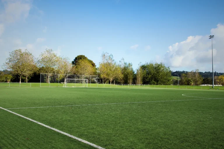 Empty football pitch with goalposts and green grass under a clear blue sky