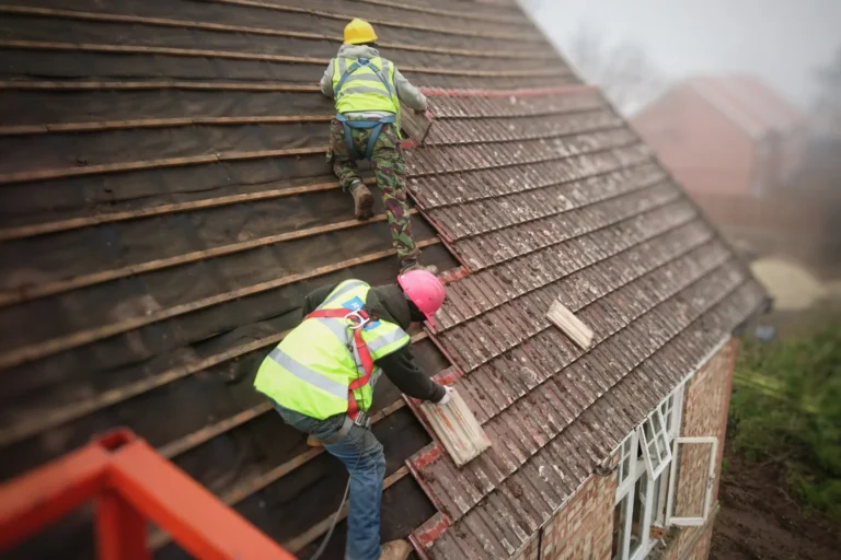 Two workers installing roof tiles on a house while secured with safety gear