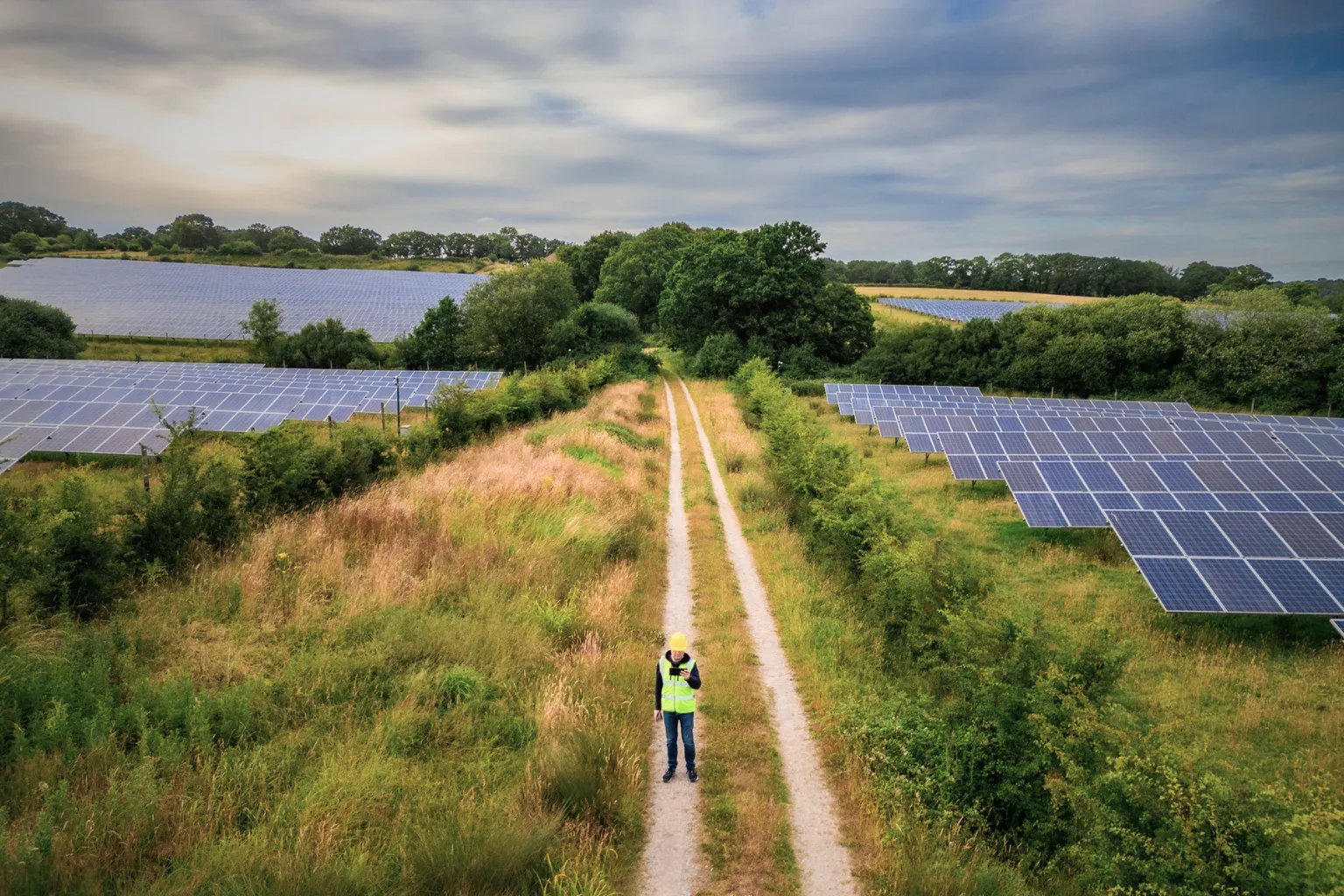 Aerial view of a solar farm with a worker inspecting the site along a rural track
