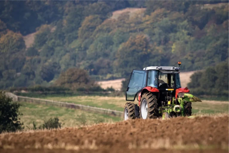 Red tractor working on a field in the countryside with hills and trees in the background