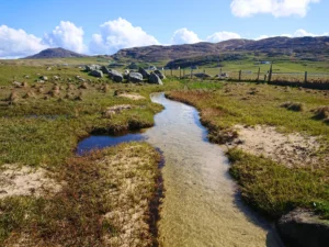 image of a winding stream flowing through a rural landscape with hills and scattered rocks